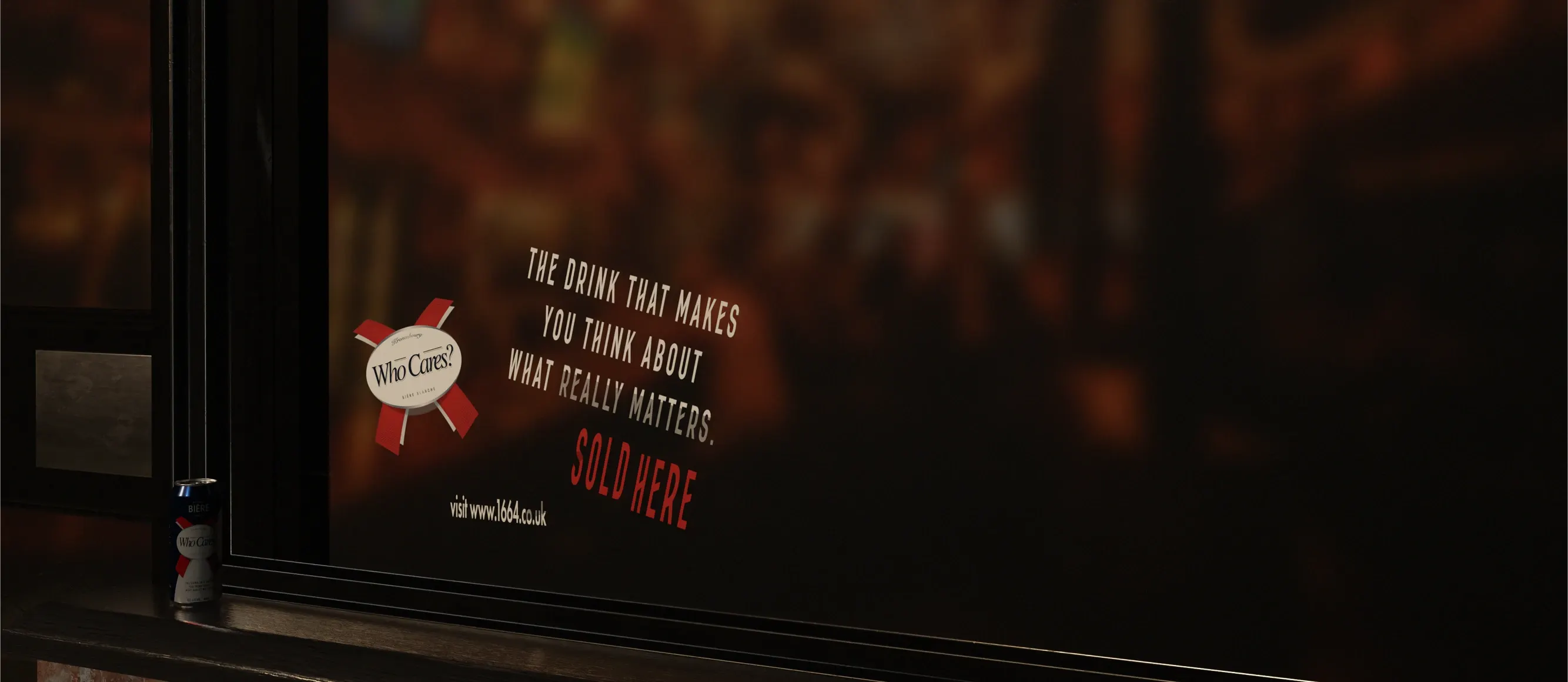 Pub window at night with 'Who Cares?' window stickers: 'The drink that makes you think about what really matters. Sold here.'